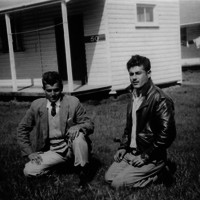 Image: two men kneeling on grass in front of buildings