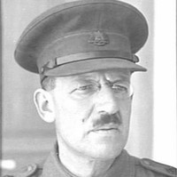 Image: A moustachioed middle-aged Caucasian man in an Australian Army officer's uniform. He is wearing a hat and spectacles with oval lenses