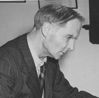 Image: A middle-aged, clean-shaven Caucasian man in a 1950s vintage pin-striped suit sits at a desk and writes on a piece of paper. He appears to be deep in thought as he writes