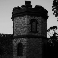 Image: A two-storey octagonal stone tower set within a high wall with a crenellated parapet.