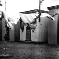 Image: clothesline in front of small, corregated iron buildings.