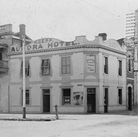 Image: A white, two-storey building stands at the corner of two dirt streets. The words ‘Aurora Hotel’ are painted on the side of the building 