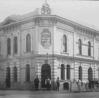 Image: sepia shot of building facade, with three men at the entrance, one by the side, and a horse-drawn carriage