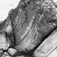 Black and white photo of large rock with words scratched deep on in its face