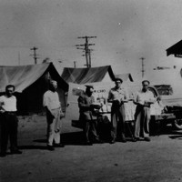 Image: group of men in front of tin huts