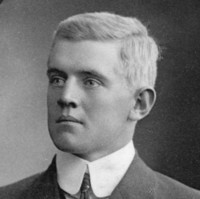 Image: A photographic head-and-shoulders portrait of a young Caucasian man wearing an early Edwardian suit. He is clean shaven and has light-coloured hair and eyes
