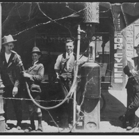 Two men and a boy with one of Adelaide's first petrol pumps, one with the hose in his mouth