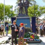 Image: men shaking hands in front of bronze sculpture of soldiers