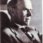 Image: A photographic head-and-shoulders portrait of a balding, middle-aged man in profile. He is wearing a mid-twentieth century suit and reading a document