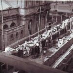 Image: A group of men lay bricks on the roof of a large building.