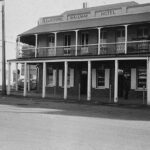 Image: A two-storey late Victorian-era building stands at the corner of two paved streets. The name ‘L.C. & N.I. Prime Railway Hotel’ is painted at the top of the building. A 1960s vintage car is parked next to the building