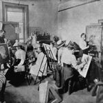 Image: A group of women in Edwardian attire paint at easels in a large, open room