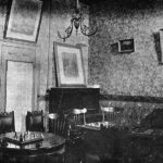 Image: Three chess tables with chairs stand in a room decorated with wallpaper and framed portraits