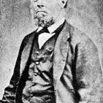 Image: A balding middle-aged man in a suit poses for a photograph. He has a deep frown on his face