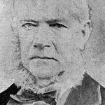 Image: A photographic portrait of a middle-aged man with white hair and large, mutton-chop sideburns