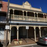 Image: two story brick building with painted ironwork and veranda