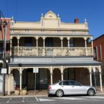 Image: two story brick building with painted ironwork and veranda