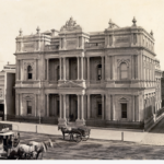 Image: horse carts and tram in front of ornate bank building