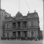 Image: horse carts and car in front of ornate bank building