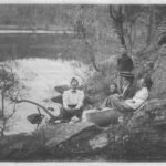 Image: Three women and two boys have a picnic on the banks of a river.