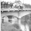 image: crowds around a car crashed through bridge railings