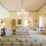 Image: A large, well-lit room containing couches and chairs next to a large fireplace