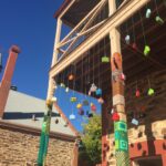 Image: coloured knitted suitcases dangle from a balcony