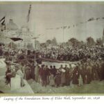 Image: A large group of people gather around a stage watching the foundation stone of Elder Hall being laid.