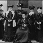 Image: photo of six women wearing black hats and dresses