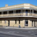 Image: A cream-coloured two-storey building with upstairs verandah. A sign over the front door reads ‘McGrath’s British Hotel’