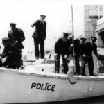 Image: A group of policemen stand on a small motor boat. One of the policemen is pointing and directing others to perform specific activities