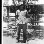 Image: A man in an Australian Army uniform stands in front of a wooden fence