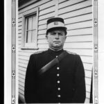 Image: A man in a police uniform with kepi cap and leather bandolier