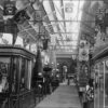 Image: A line of displays fill a large hall. In the foreground of the photograph a glass cabinet topped with a large wooden horse holds leather harnesses and other tack.