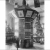 Image: a decagonal display featuring bottles of wine and spirits sits upon artfully arranged barrels. The top of the display features pictures of people and scenes. On either side of the display two others, pyramidal in shape, display similar products.