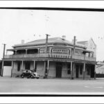 Image: a two storey corner hotel with balcony. A 1940s era car is parked outside. Signs on the upper level advertise West End Exhibition Stout and Seppelts wine.