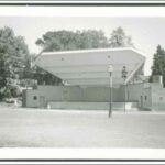 Image: A raised stage in surrounded by parklands with an angular shell shaped roof