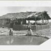 Image: Three men gather around a pool in front of a wooden framed building with a half mud-brick wall and thatched roof.