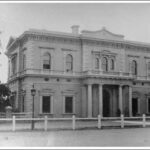 Image: Front of large, two-storey historic building with columns bordering its front door