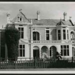 Image: A two storey house with a pitched roof, decorative gable, bay windows and a arched verandah/balcony