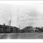 Image: a wide city street with single and double storey buildings one of which has a cupola