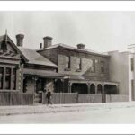 Image: a man walks down a street of terraced buildings including a single storey stone villa on the left, a two storey house in the centre and a 1920s "modern" commercial building on the right