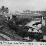 Image: a bridge with an arched parapet spans a small river in a deep valley