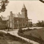 Image: Black and white photograph of two-storey stone house at the top of a hill