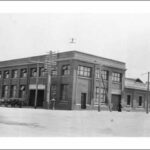 Image: a two storey brick factory with open windows on its upper floor. A horse drawn wagon stands next to the large entranceway.