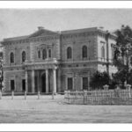 Image: Front of large, two-storey historic building with columns bordering its front door