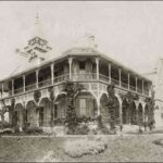 Image: Black and white photograph of two-storey stone house with wrap-around verandas on both levels