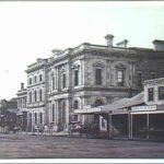 Image: a large two storey stone public building with arched windows on the ground floor and rectangular windows with triangular pediments above. The entrance to the building is recessed and flanked by columns