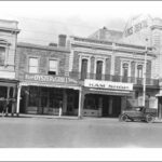 Image: a row of two and three storey commercial buildings with verandahs and/or balconies including the Crown and Sceptre Hotel, the Fish, Oyster and Grill Saloon, A.F. Shelton's Ham Shop and the King's Theatre.