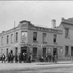 Image: A group of men stand outside a two storey corner hotel. Signs name it the Stag Inn and advertise Walkerville Ales for sale.